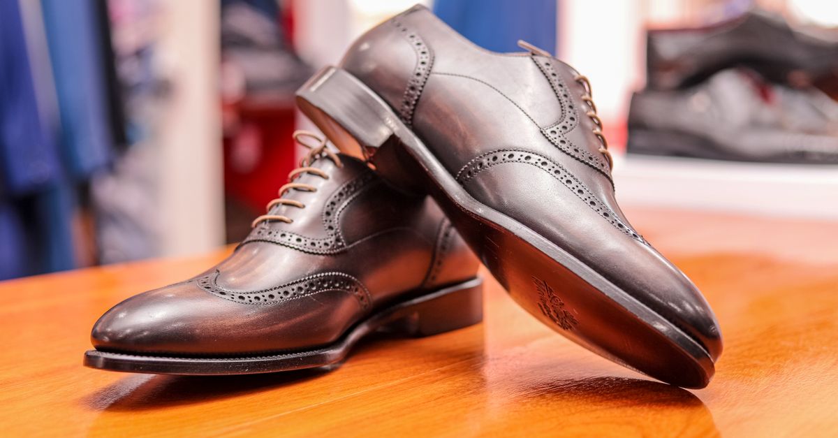A pair of polished dark brown leather Oxford brogues resting on a wooden table.
