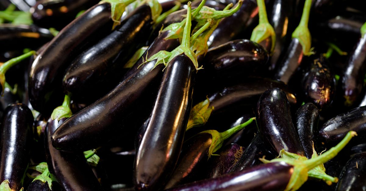A pile of glossy deep purple eggplants with green stems, photographed close-up.