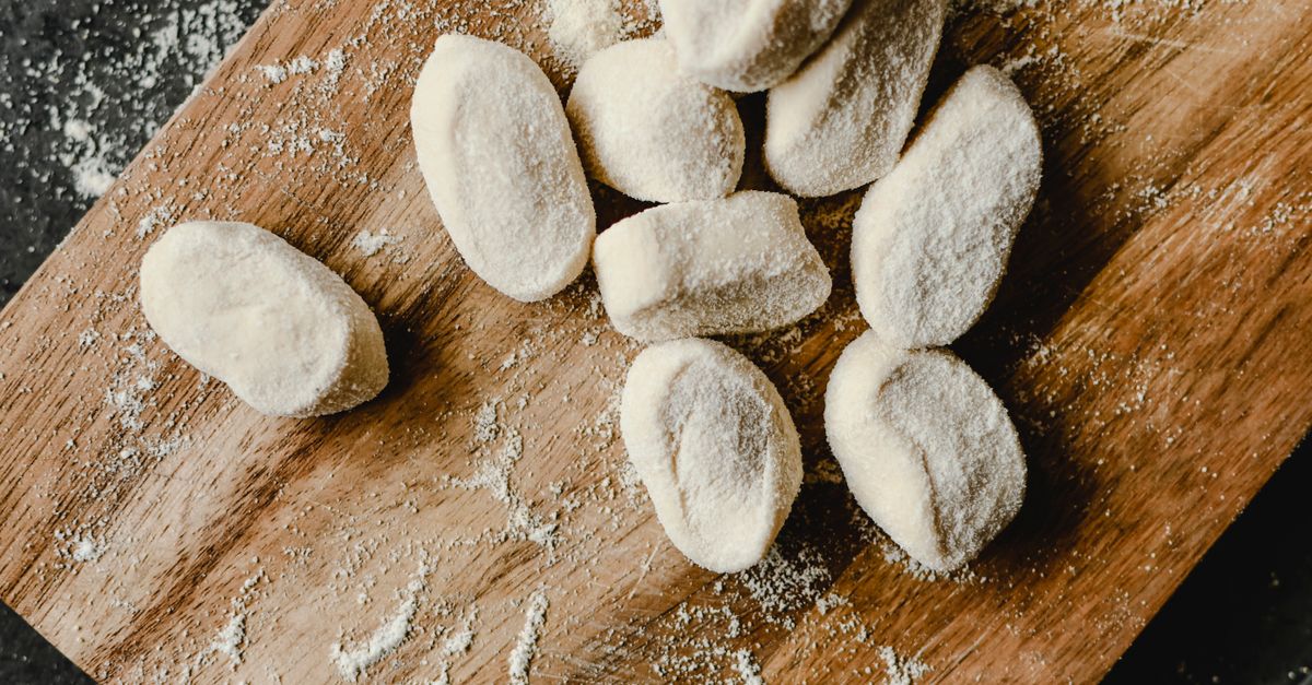 Overhead view of raw dough pieces dusted with flour arranged on a wooden board.