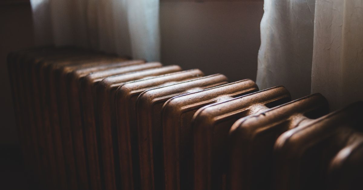 Close-up of a cast-iron radiator's ridged sections glowing in warm light with curtains in the background.