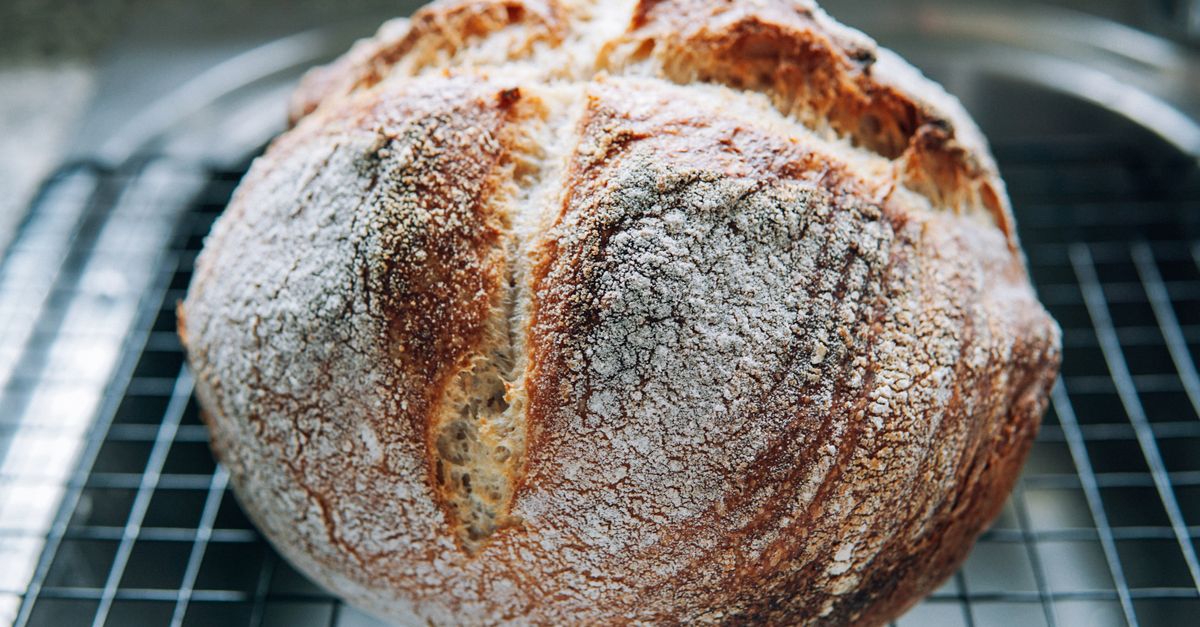 A round, flour-dusted crusty sourdough loaf cooling on a wire rack.