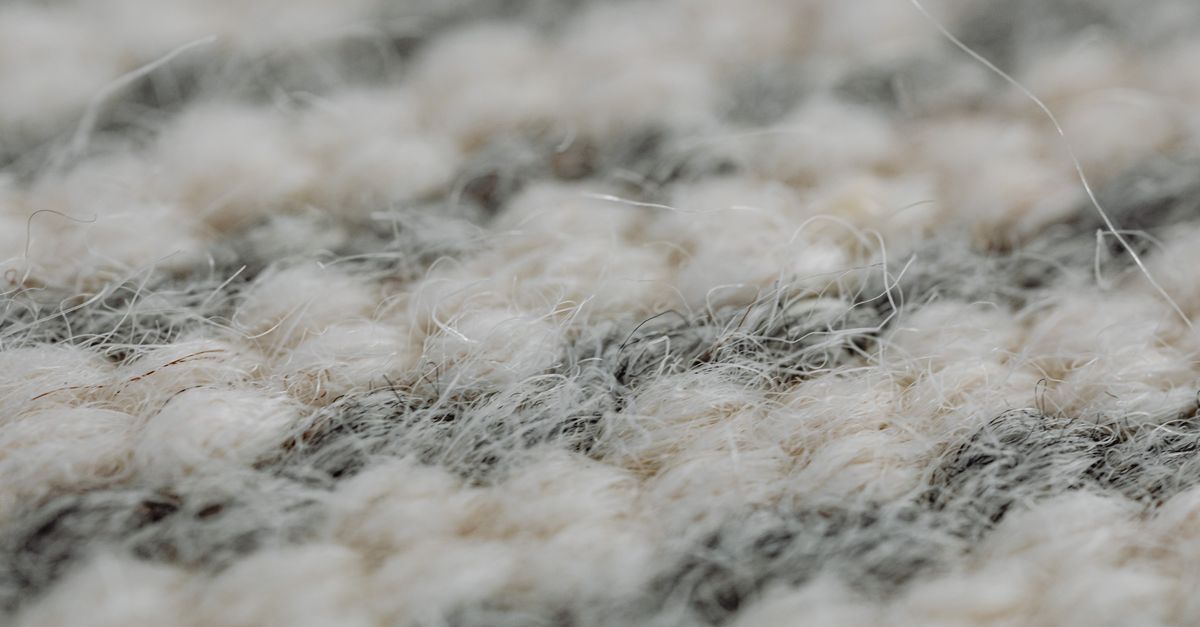 Close-up view of thick woven carpet fibers in cream and gray tones, shown without any powder sprinkled on them.