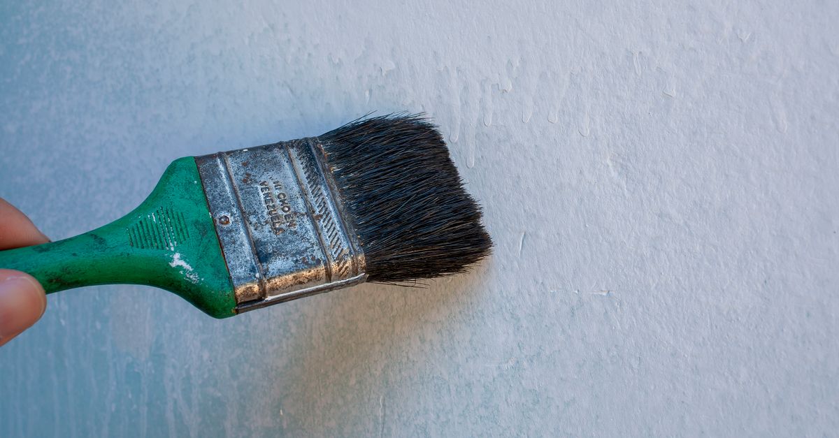 A green-handled paintbrush with worn bristles rests against a light blue textured wall.