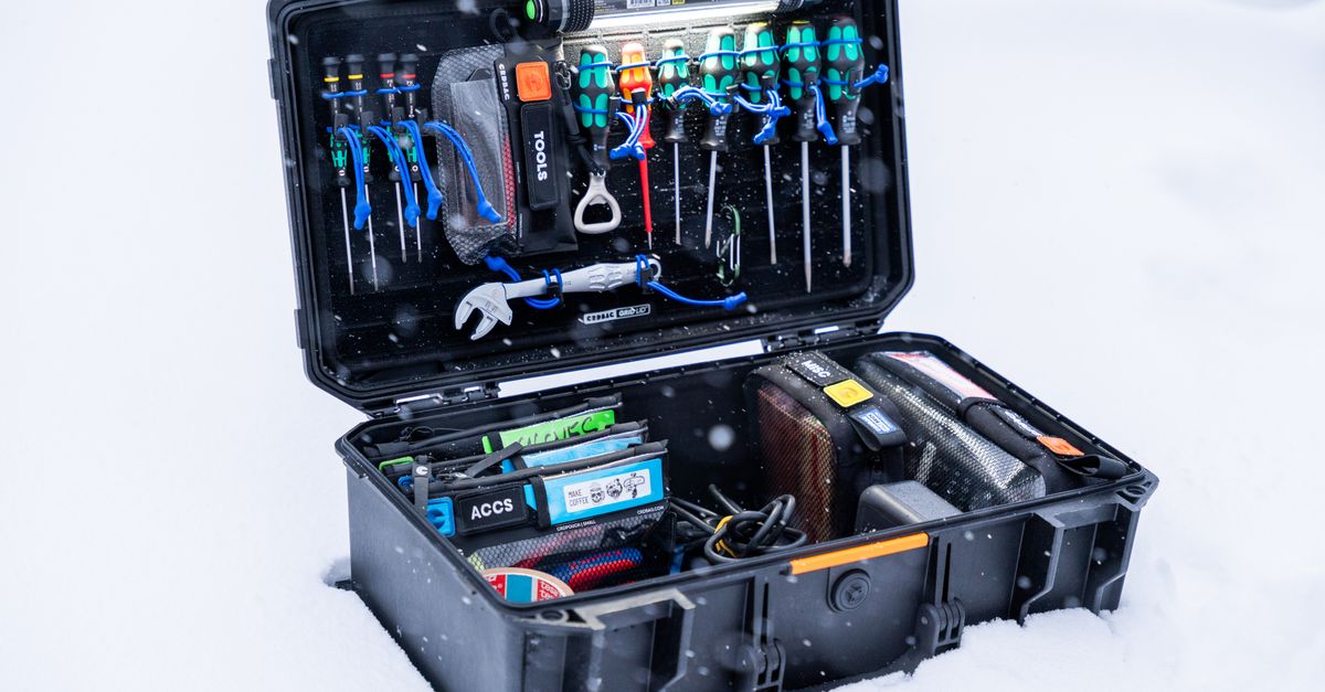 An open black rugged case sitting in snow, packed with tools, screwdrivers, a wrench, and organized supply pouches.