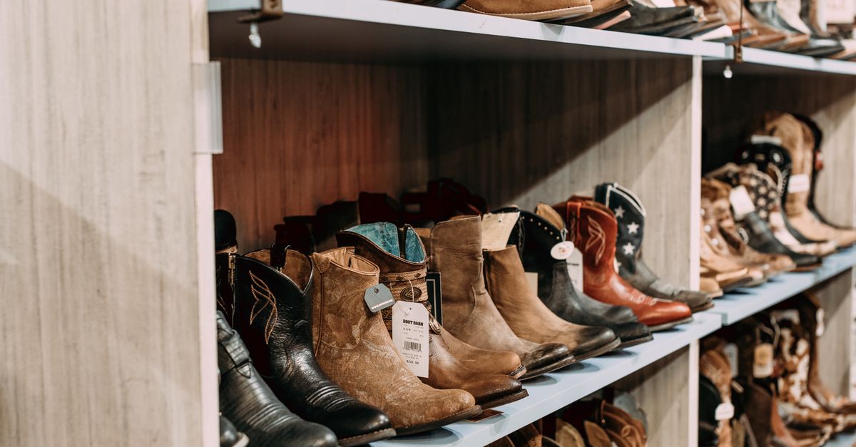 Rows of leather boots displayed on wooden shelves with price tags attached.