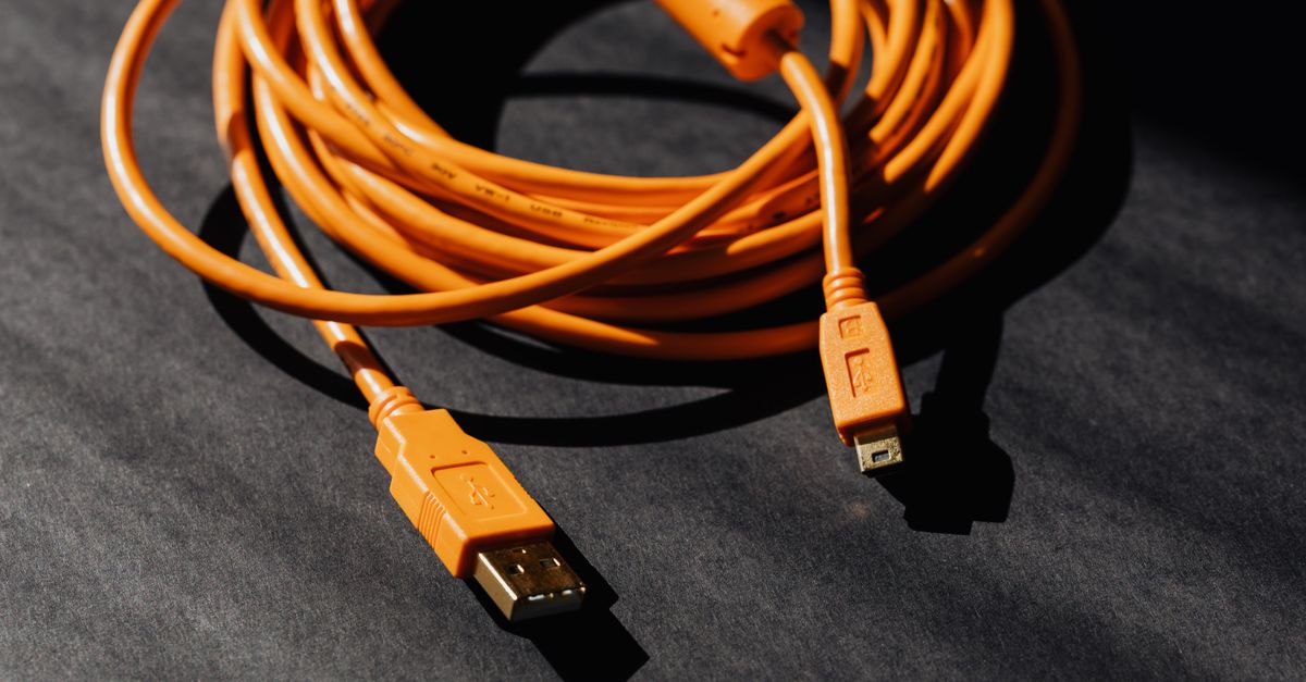 An orange extension-style cable neatly coiled on a dark textured floor, with its plug and connector ends visible and undamaged.