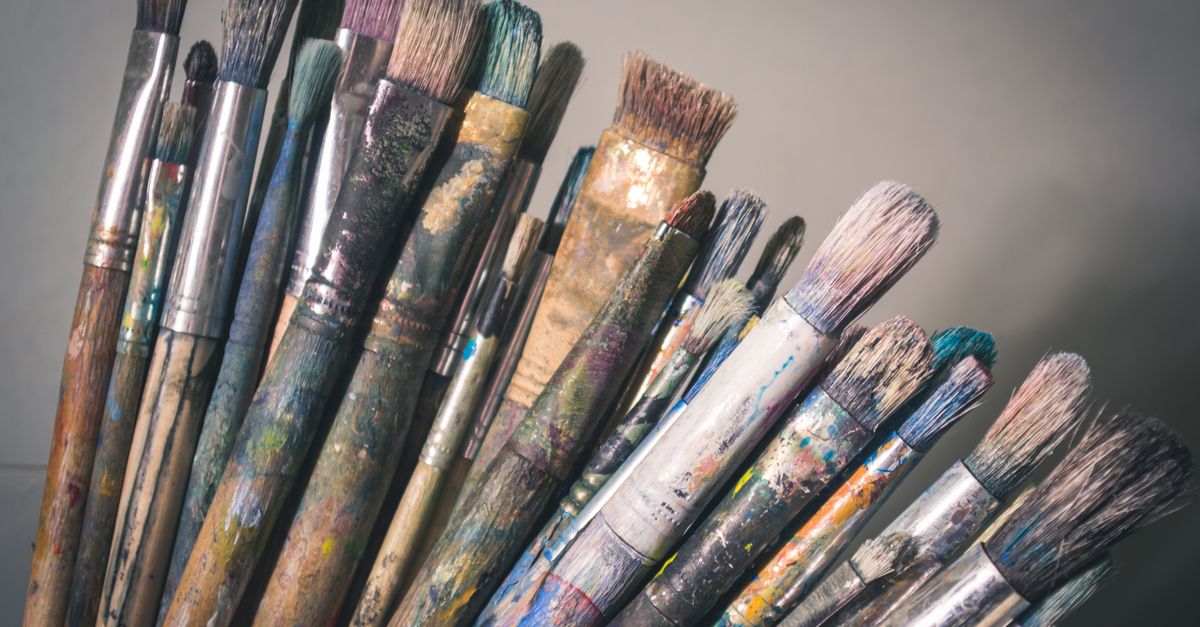 A cluster of paint-stained artist brushes with various bristle shapes standing upright, showing dried paint residue on their handles and ferrules.