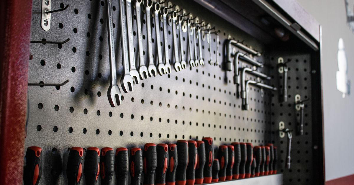 A pegboard tool panel neatly organized with hanging wrenches, hex keys, and a row of screwdrivers with red and black handles.