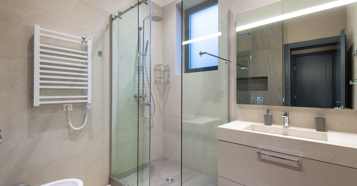 A modern bathroom with a glass-enclosed shower stall, a white towel radiator, and a sink vanity, but no squeegees visible.