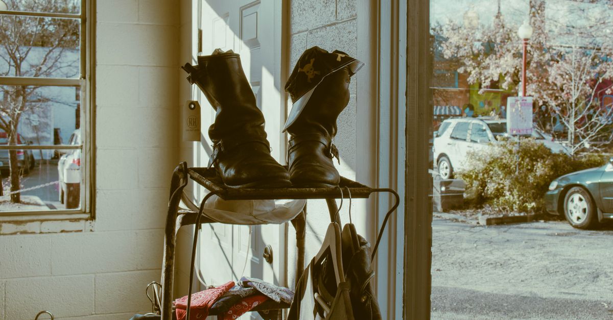 A pair of black boots resting on a small metal rack near an open front door with a view of the street outside.