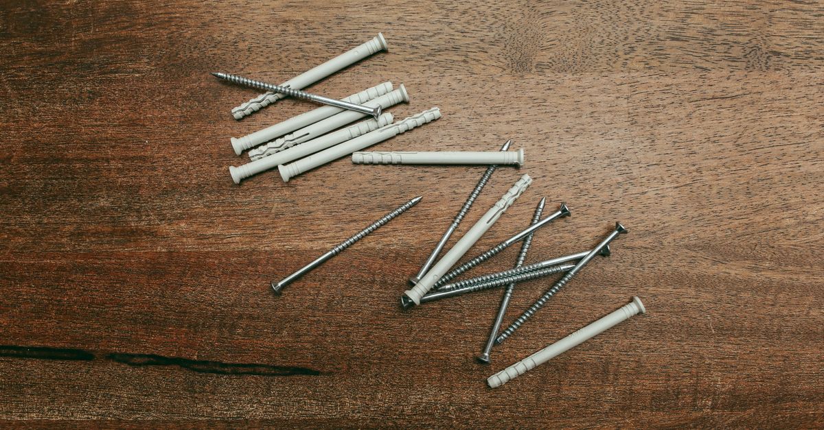 An assortment of wall anchors and screws scattered on a dark wooden surface.