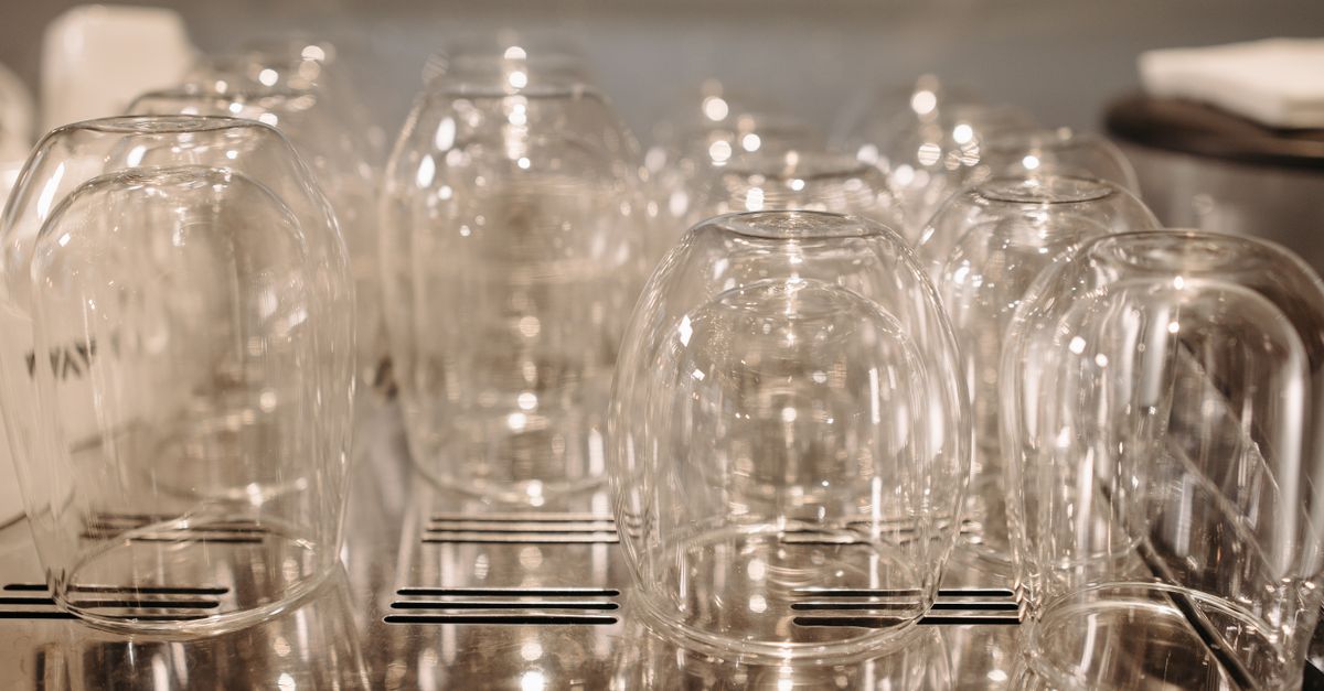 Rows of clear glasses arranged upside-down on a dishwasher rack for drainage