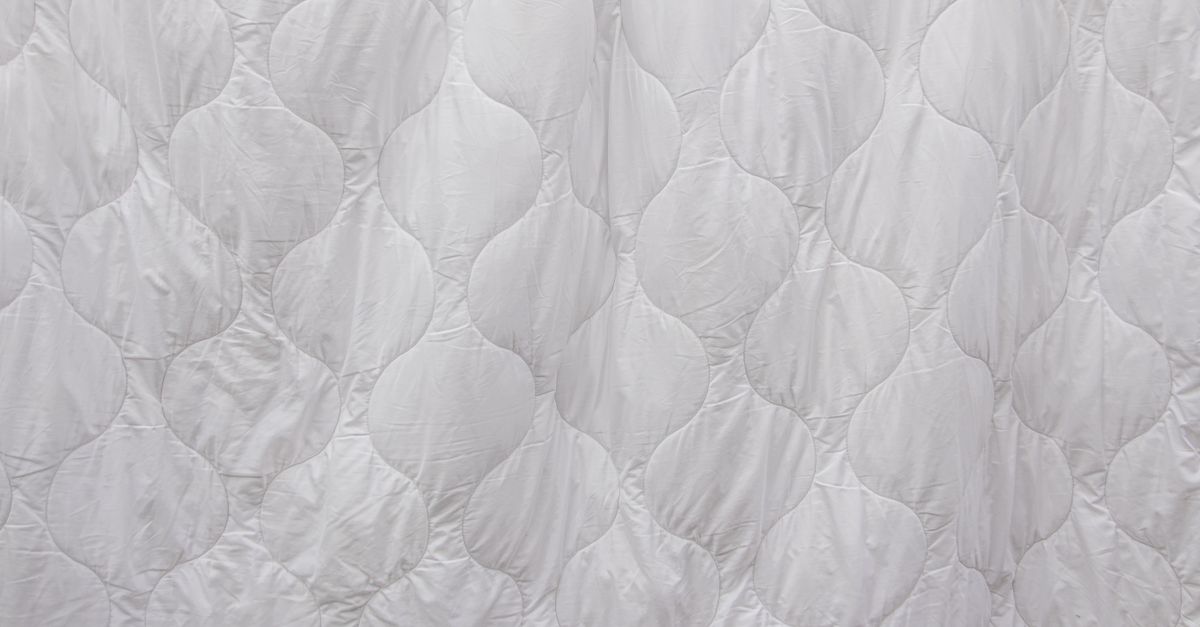 A close-up of a white quilted duvet with a smooth wave-patterned stitching and no visible wrinkles.