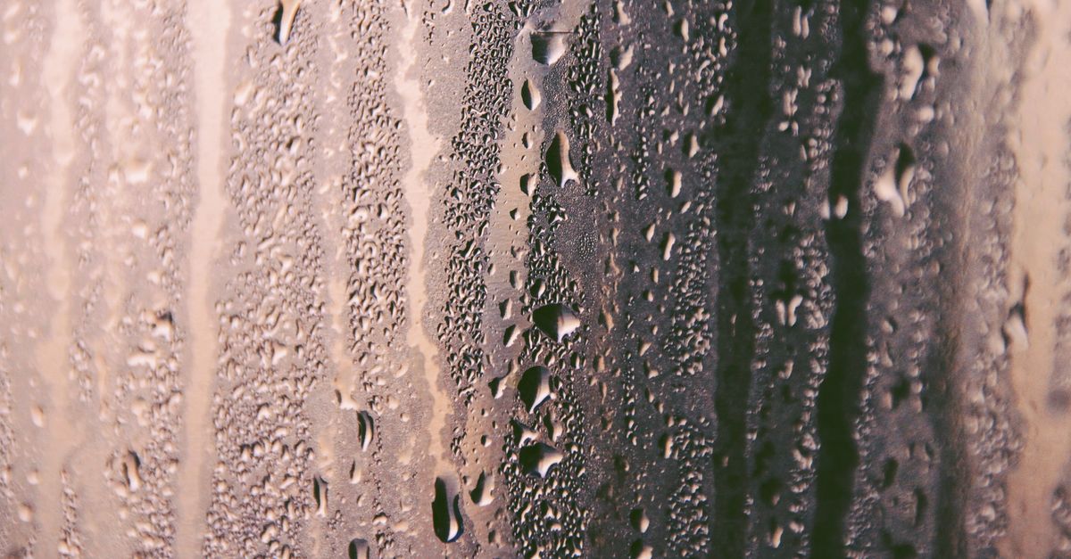 Close-up of water droplets and streaks of condensation running down a cold glass pane, with streaky rivulets forming against a muted background.