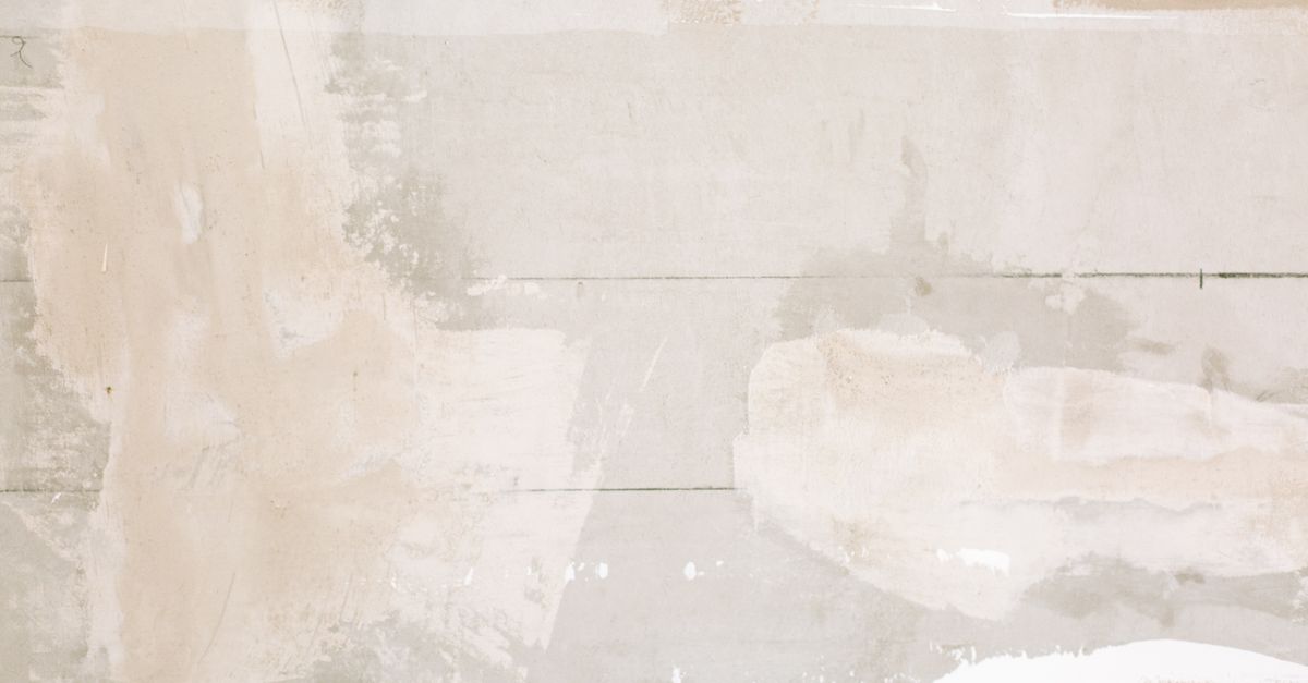 A close-up of a textured, patched wall surface with uneven patches of filler and paint near wooden boards.