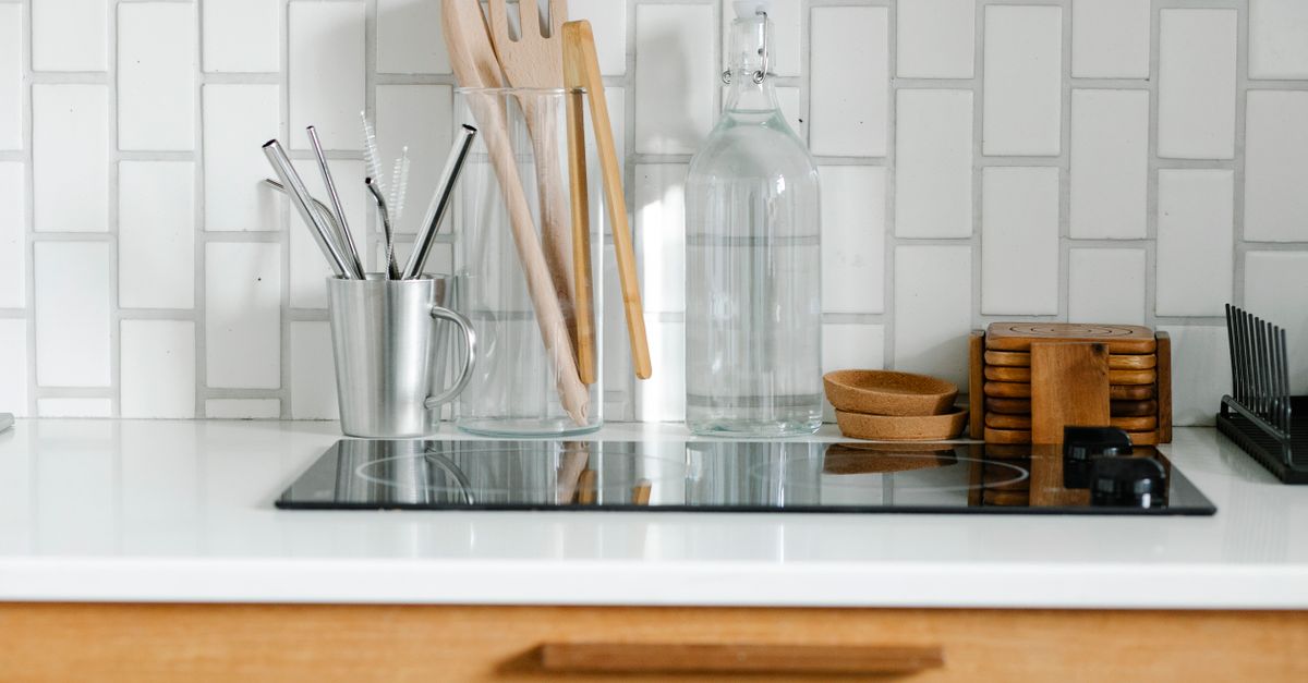 A glass-top induction stovetop on a white countertop, clean and reflective, surrounded by kitchen utensils and a glass bottle.